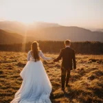 les mariés qui marchent dans un champs sous un couché de soleil, photo de dos